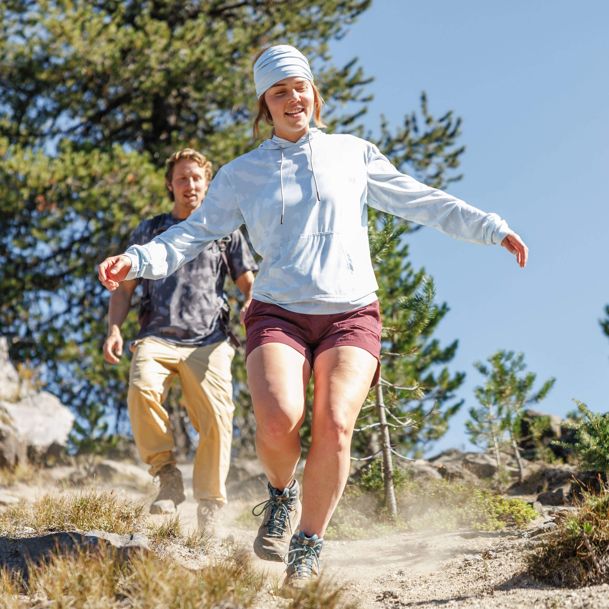 Woman hiking down a dusty mountain trail wearing the BlackStrap Women's Aspect Hoodie Long Sleeve #color_slash stratus