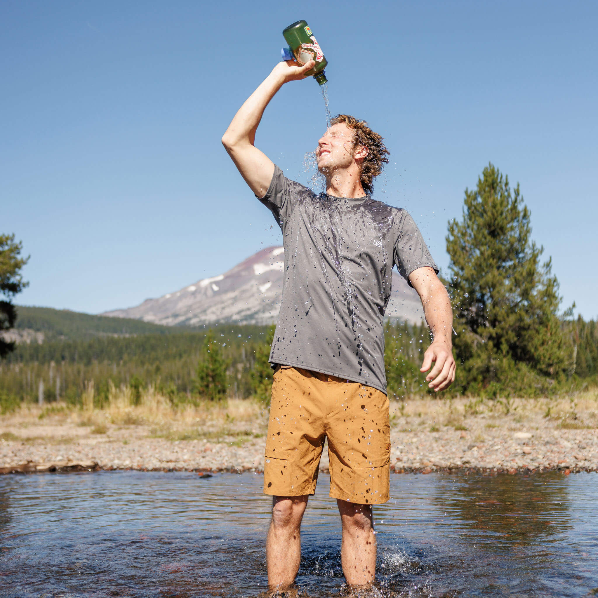 Man pouring water over his head while standing in a mountain creek wearing the BlackStrap Men's Aspect Tee #color_smoldered