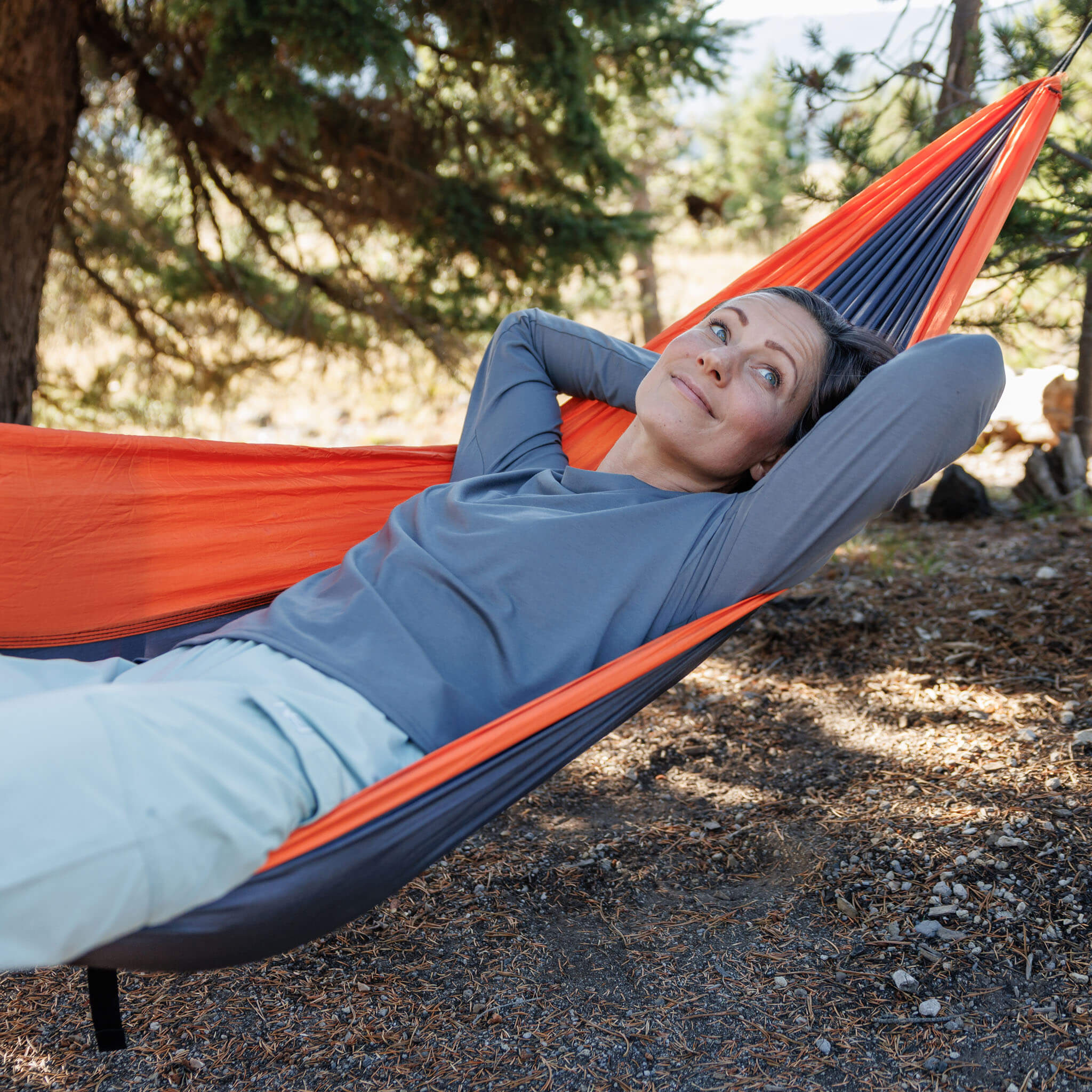Woman relaxing in a hammock in a pine forest wearing the BlackStrap Women's Aspect Long Sleeve #color_deschutes